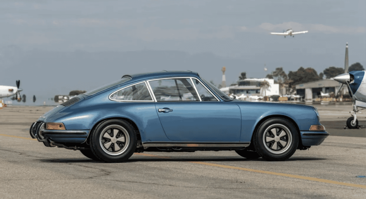 The 1971 Porsche 911S on an airport tarmac with small aircraft in the background.