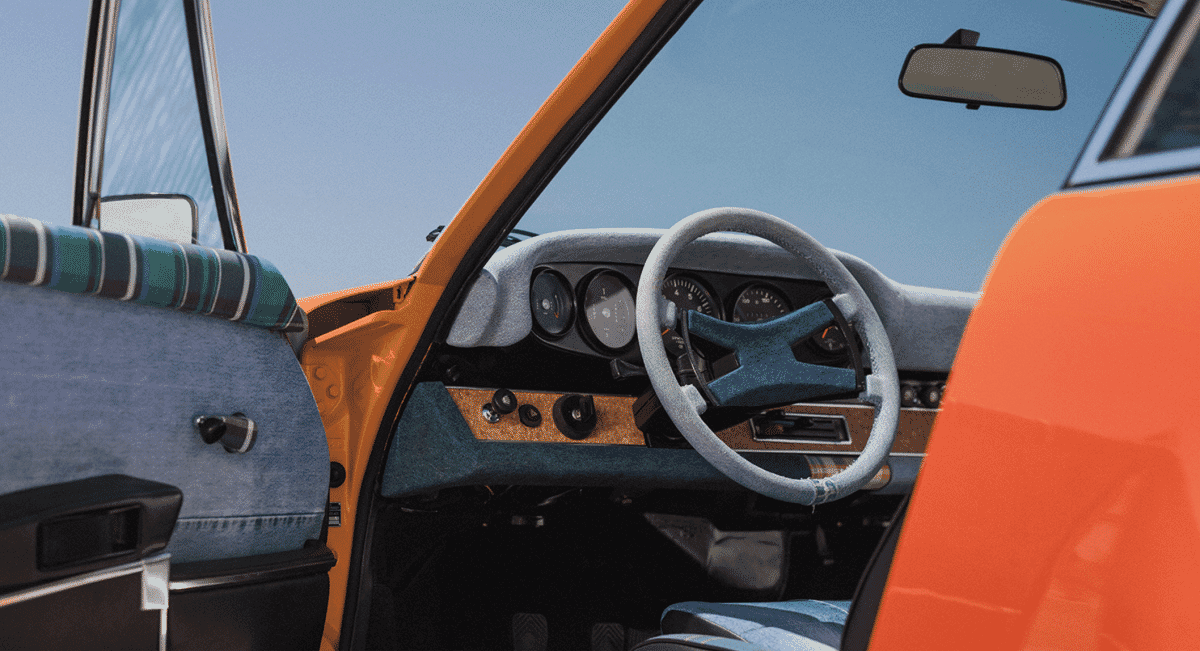 Interior view of a Porsche 911 featuring a wooden/cork dashboard, retro gauges, and blue upholstery.