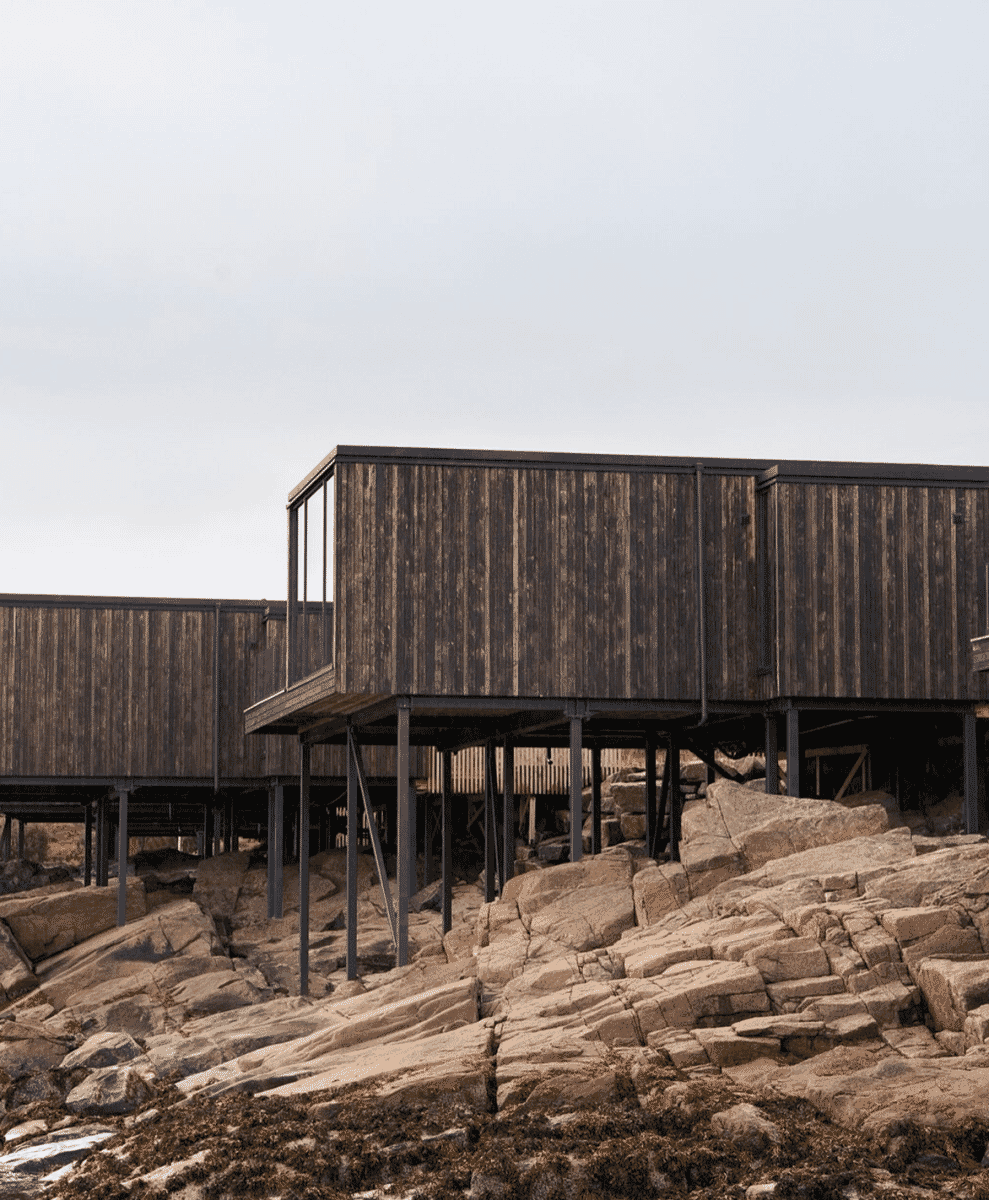 Modern wooden cabins on stilts under an overcast sky on the rocky coast of Lofoten.