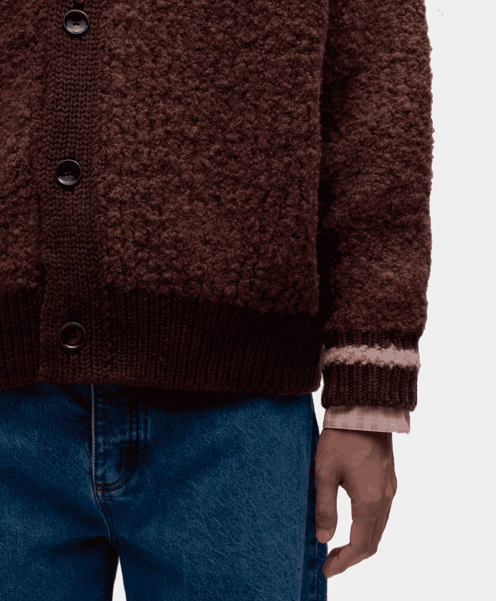 Close-up detail of a textured brown knit cardigan showing the ribbed cuffs and button alignment.