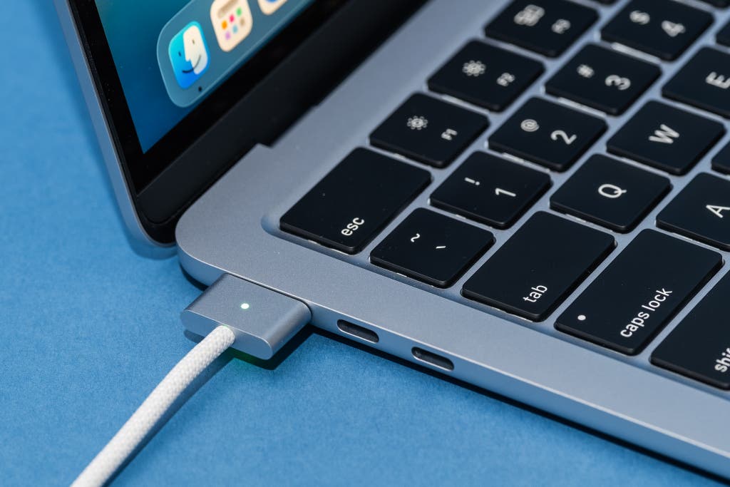 Close-up of a MagSafe charging cable connected to the side of a MacBook.