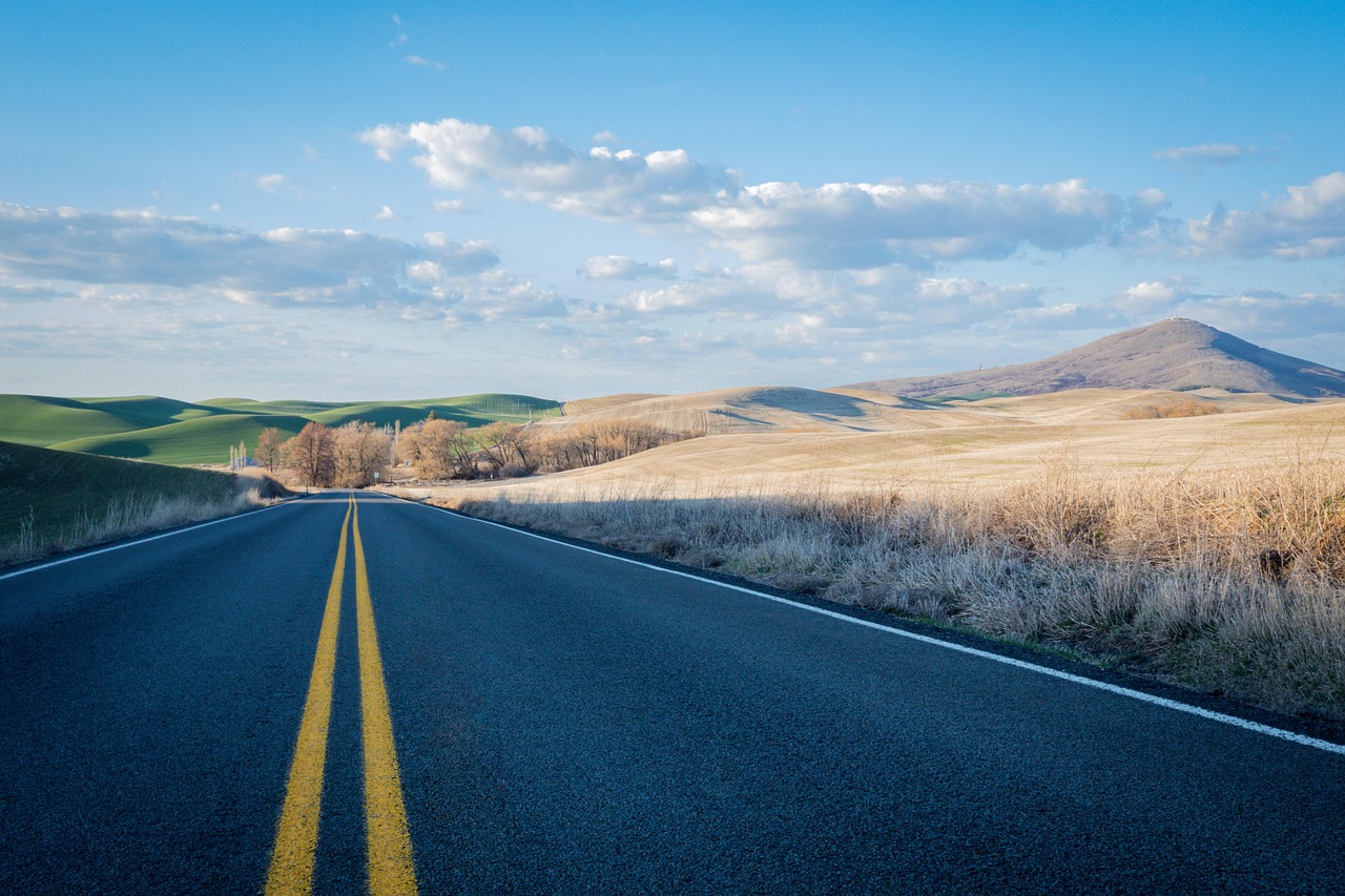A long stretch of highway leading towards towering snow-capped mountain peaks.