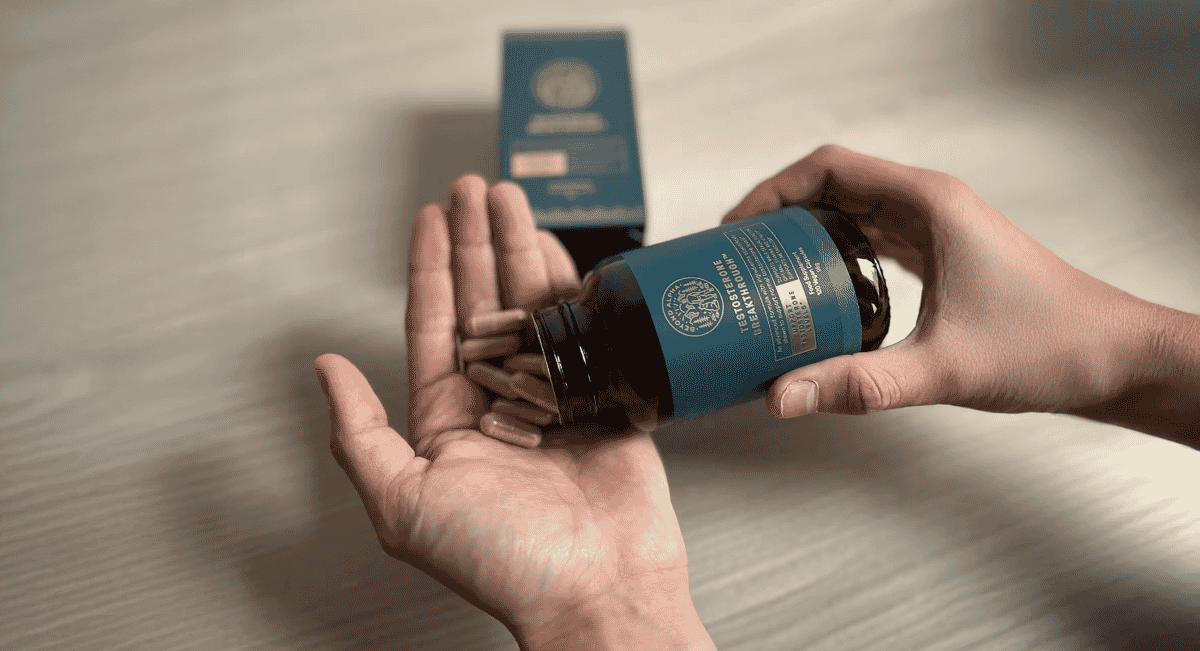 Close-up of capsules being poured into a hand from a blue supplement bottle.