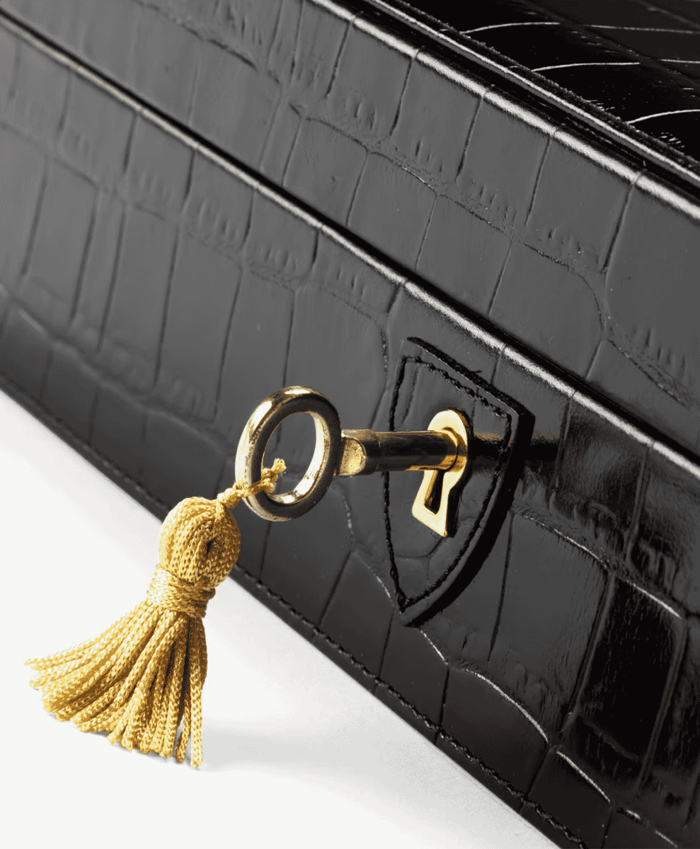 Black crocodile-textured leather watch box featuring a gold key and tassel.