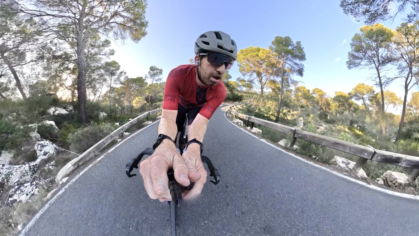 A cyclist wearing AirPods Pro 3 while riding on a paved road.