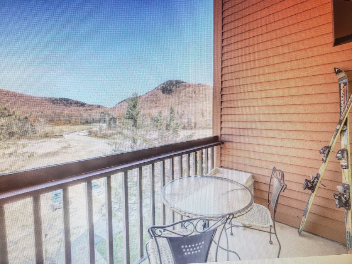 A balcony with wooden railings overlooking snowy peaks, featuring a dedicated ski storage rack.