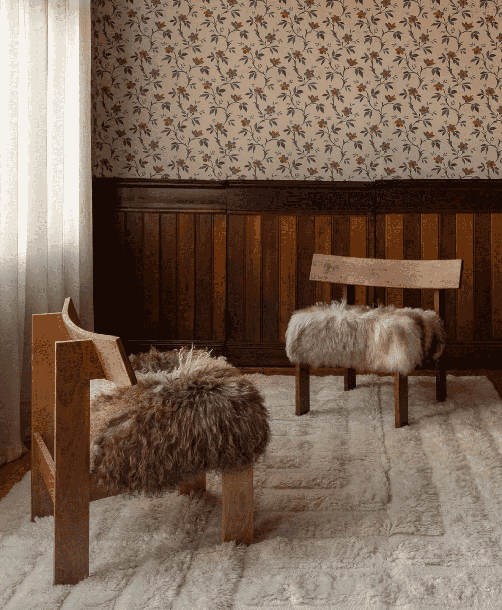 Rustic interior with wooden chairs, sheepskin, and floral wallpaper.