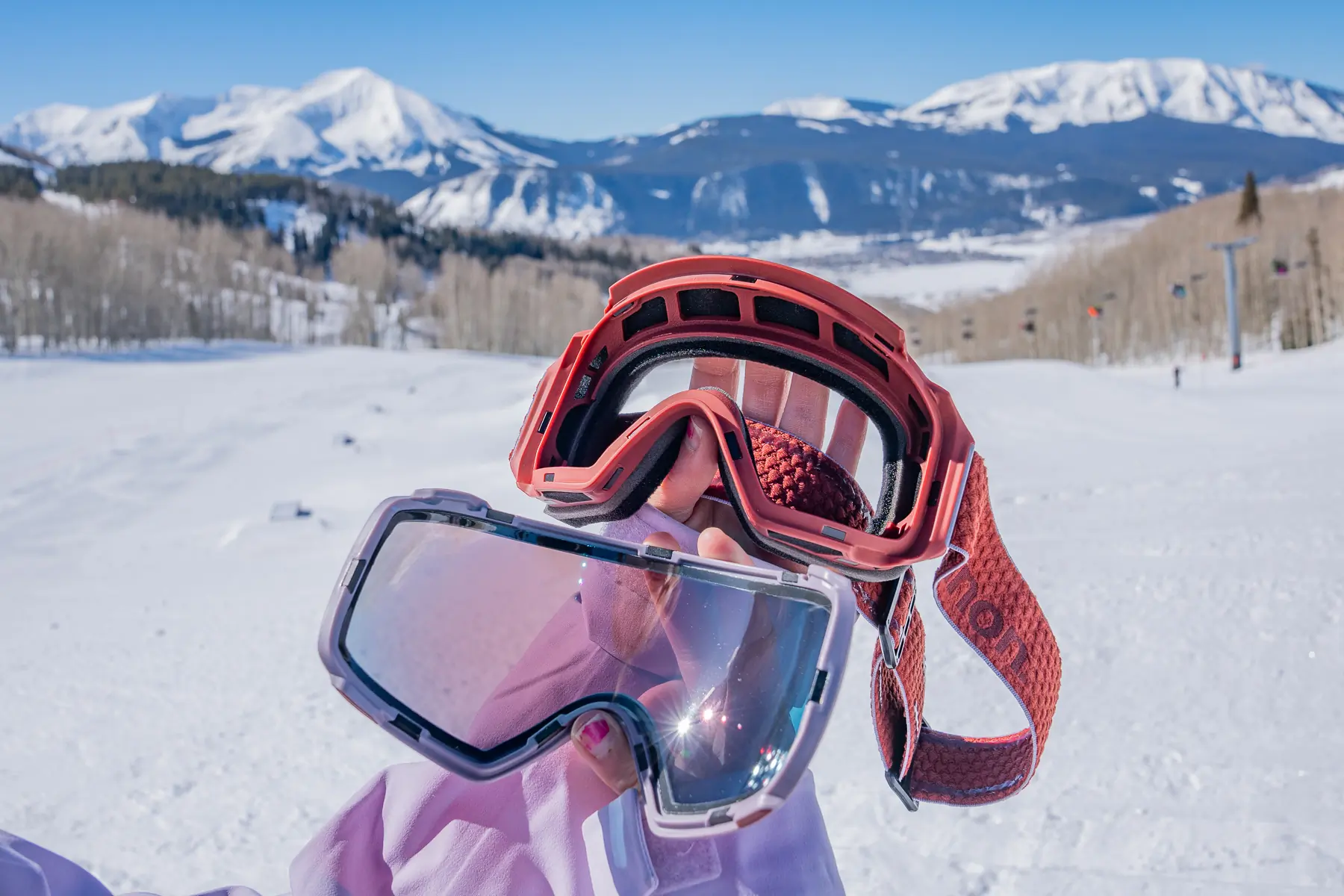 Close-up of a blue-tinted ski goggle lens and frame with a mountain reflection.