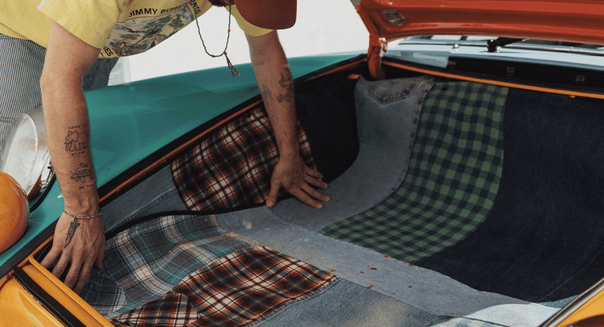 A person in streetwear leaning into a car trunk lined with colorful patchwork plaid and denim fabric.