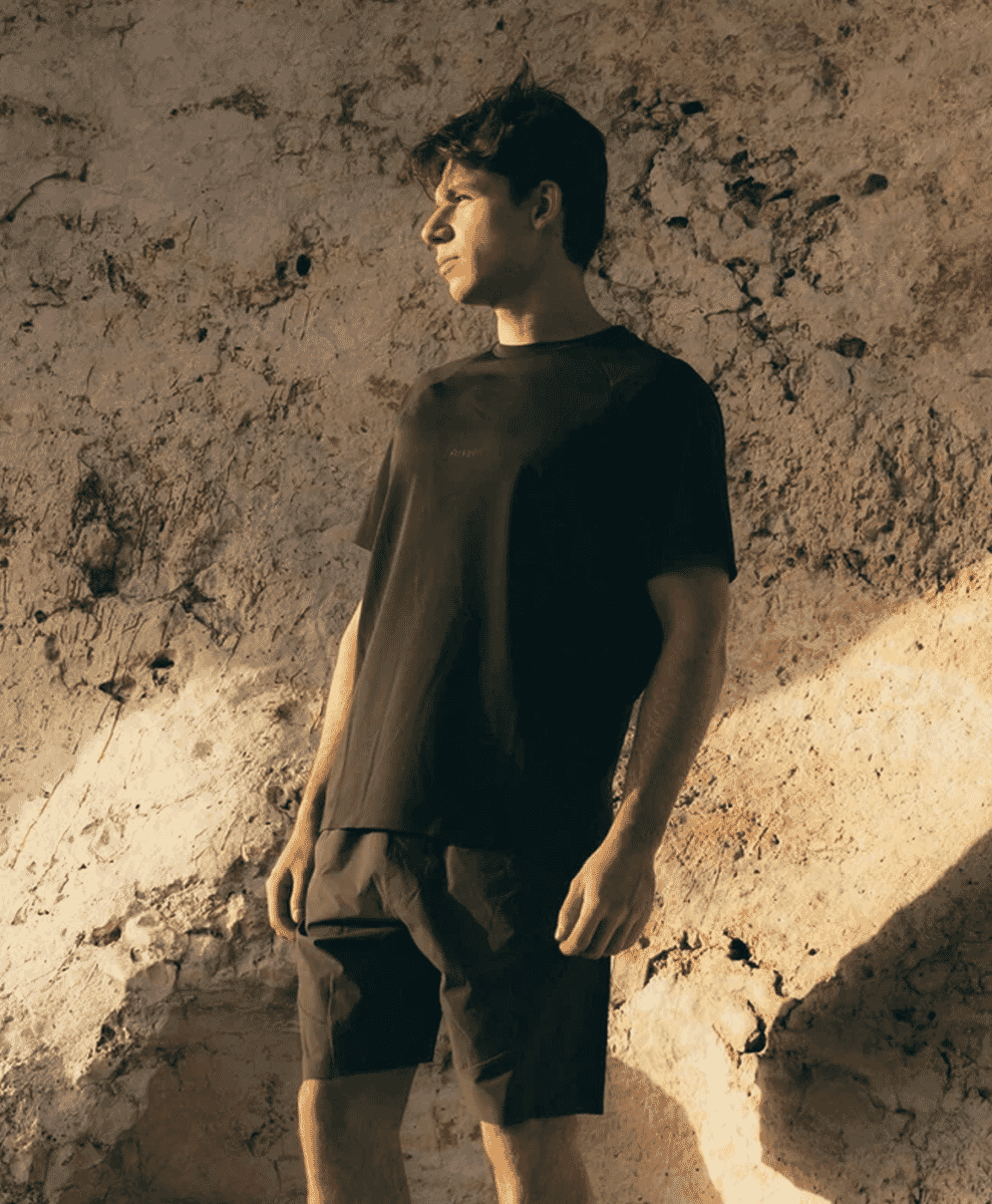 A man modeling a dark brown relaxed-fit t-shirt and shorts set against a stone wall.