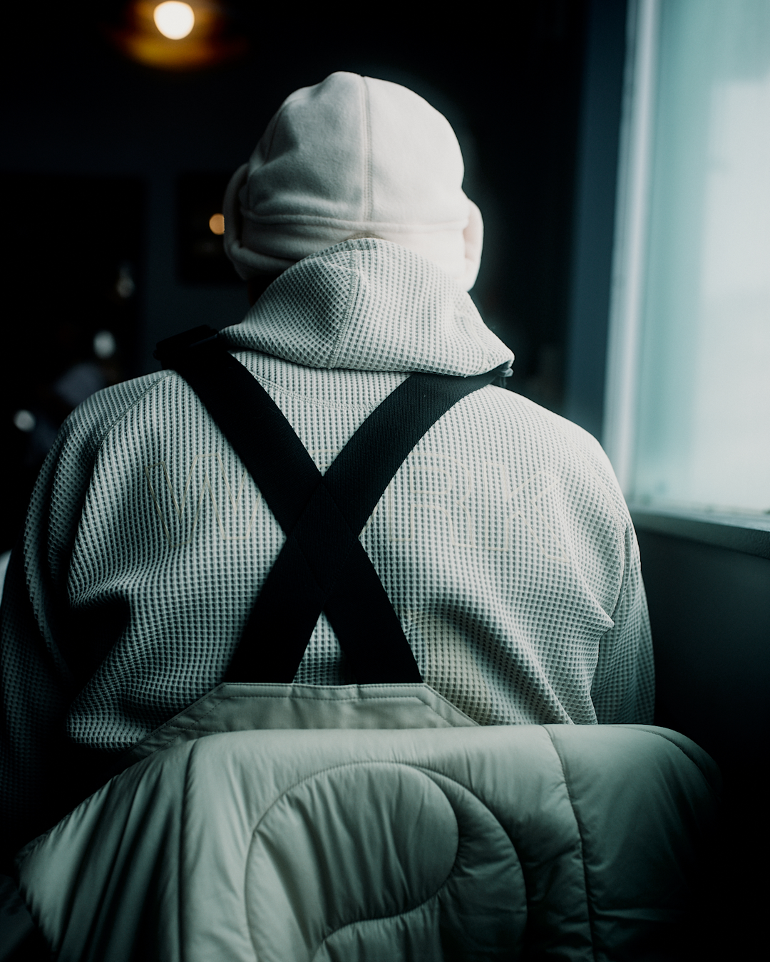 Person from behind wearing a white beanie and a textured waffle-knit hoodie with black suspenders.