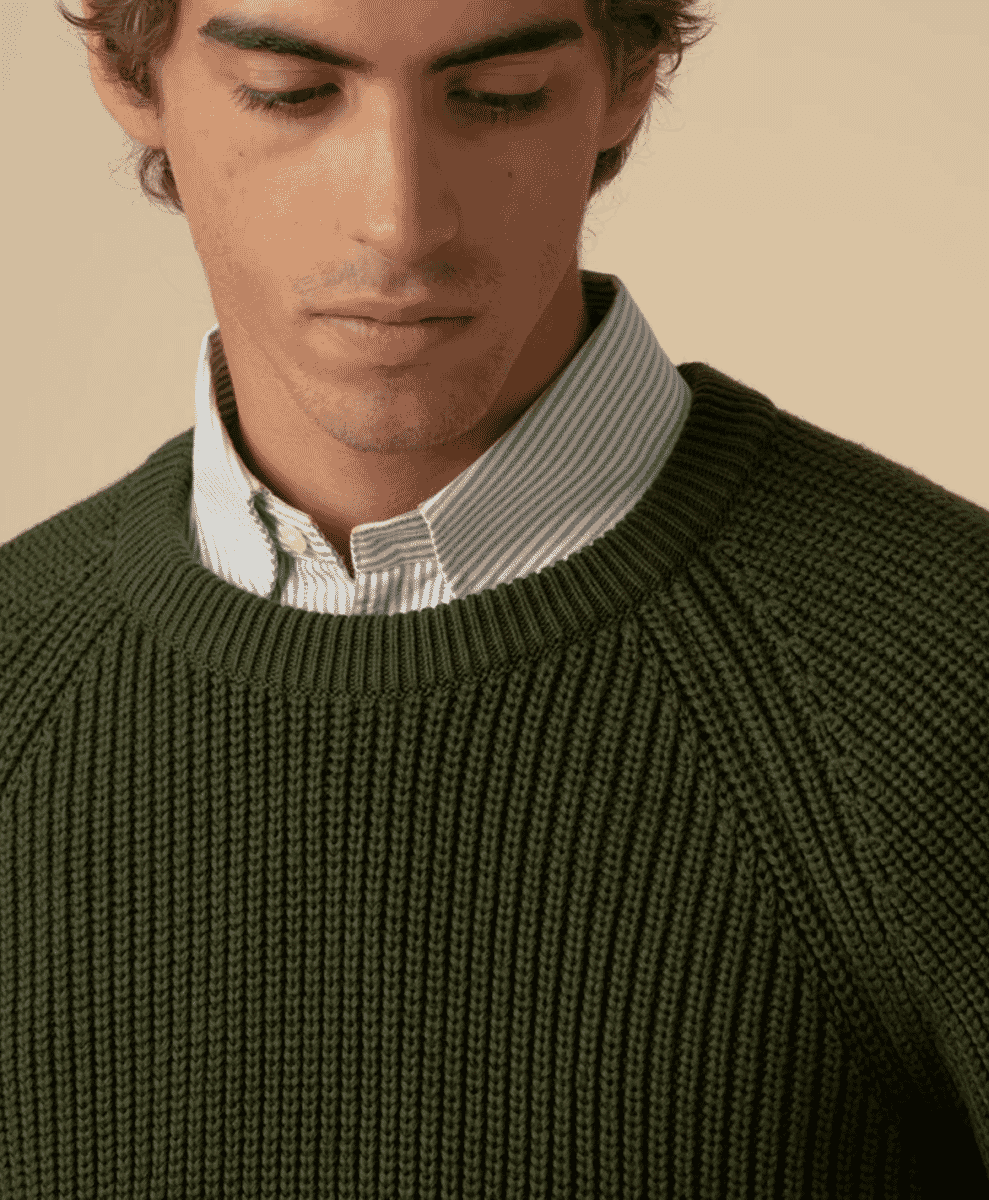 Close-up of a forest green ribbed knit sweater layered over a striped shirt.
