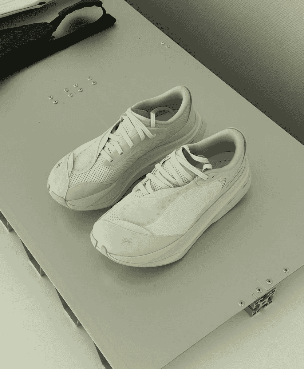 White ON running sneakers displayed on an industrial gray surface with hardware details.