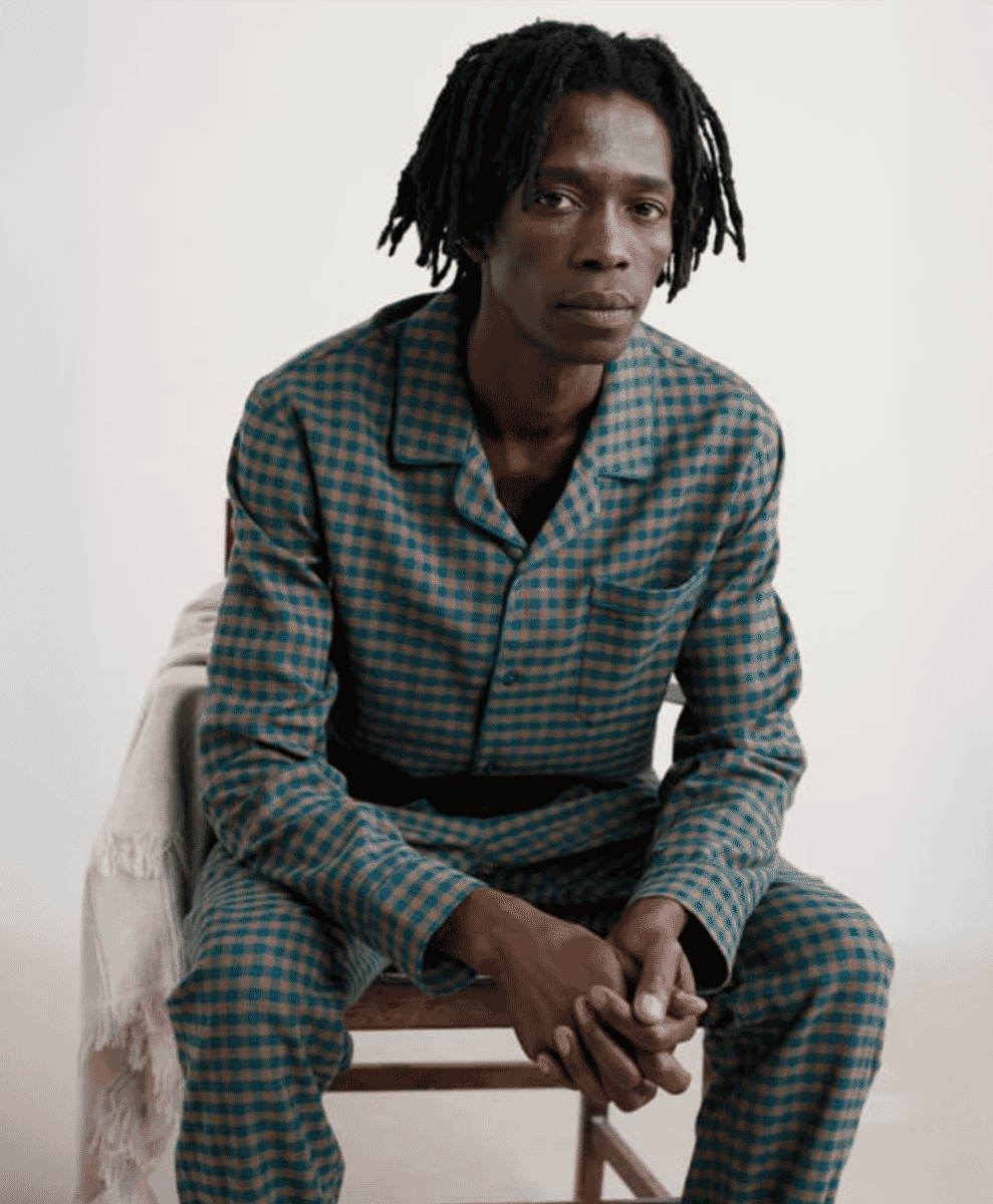 A man sitting on a wooden chair wearing a blue and beige checkered flannel pajama set.